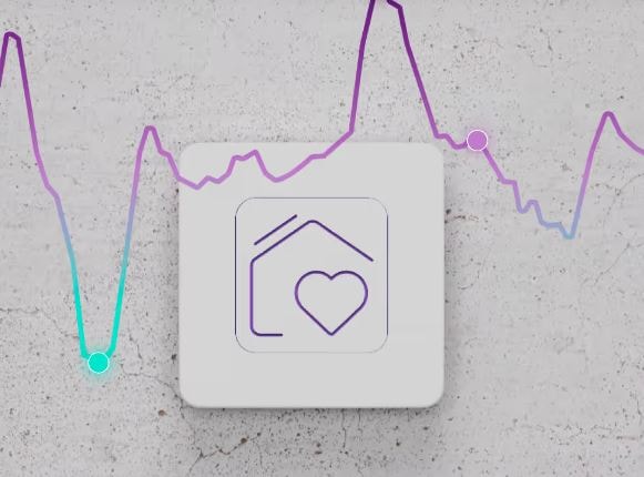 Gerät mit Haus-und-Herz-Symbol vor Betonwand, umgeben von bunter Energielinie.